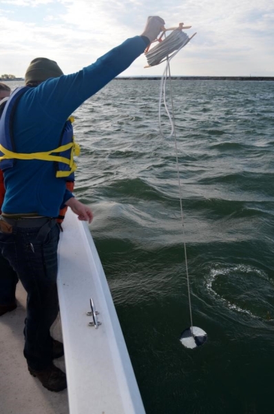 A person on a boat holds a line with a black and white patterned disk in the water.