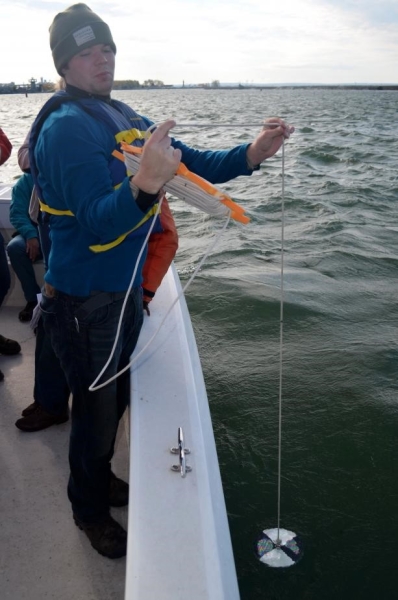 A person on a boat holds a line with a black and white patterned disk in the water, looking at a marking on the line.