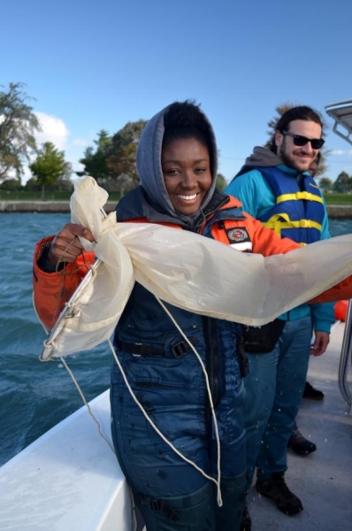 A person smiles and holds up a long cylindrical net, while another person looks on.