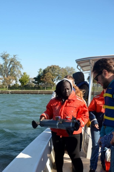 A person stands at the edge of a boat holding up a cylindrical tube while another person looks on.