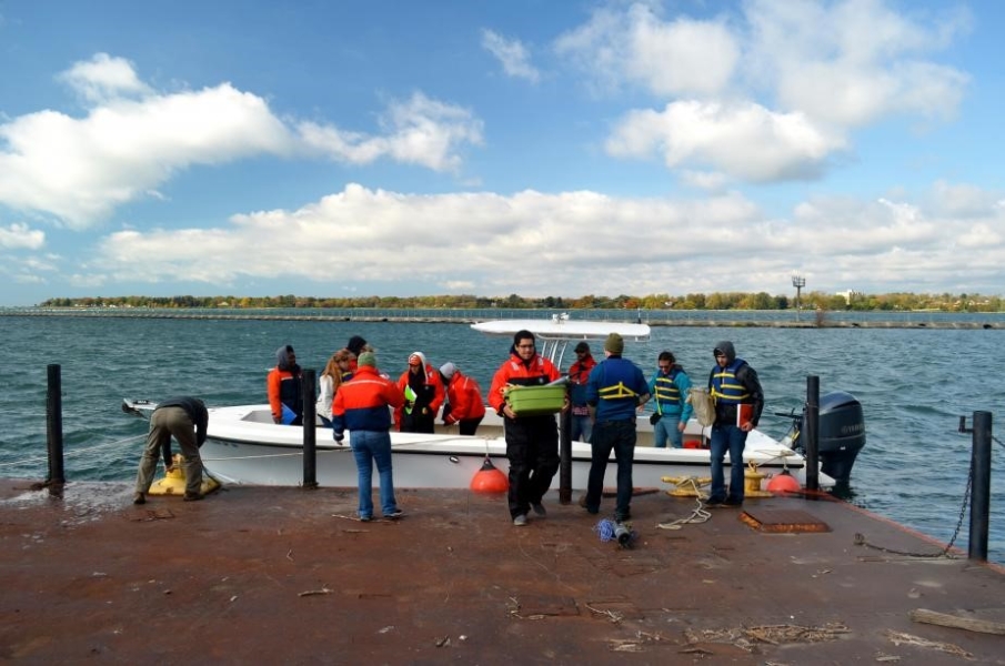 Several people on or near a boat at a dock. One is securing the boat with rope while some others carry supplies off the boat.