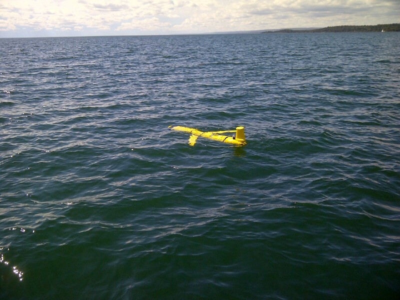 A underwater drone shaped like a plane sits at the surface of the water in a lake