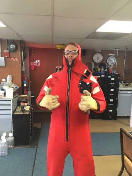 A person in a bright red safety suit gives two thumbs up inside a lab.