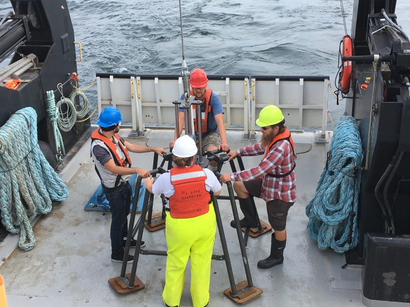 Four people stand around a metal frame on the back of a large boat.