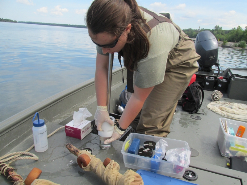 A graduate student on a boat opens a water sampler to take a sample of water. There is sampling gear around her