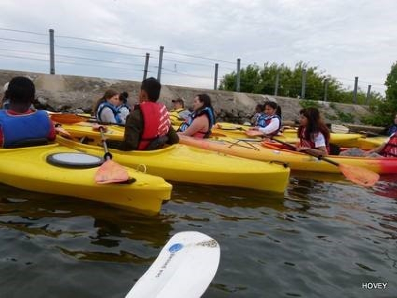 A group of people in kayaks by a breakwall.