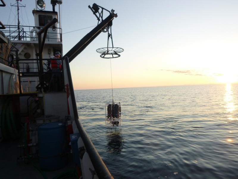 A large frame and winch is used to lower equipment into the water off the side of a large boat