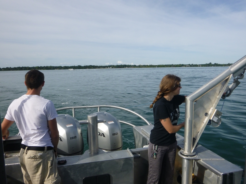 Two people working on the back deck of a boat. One person is working near a boom arm extended over the water while a second stands nearby