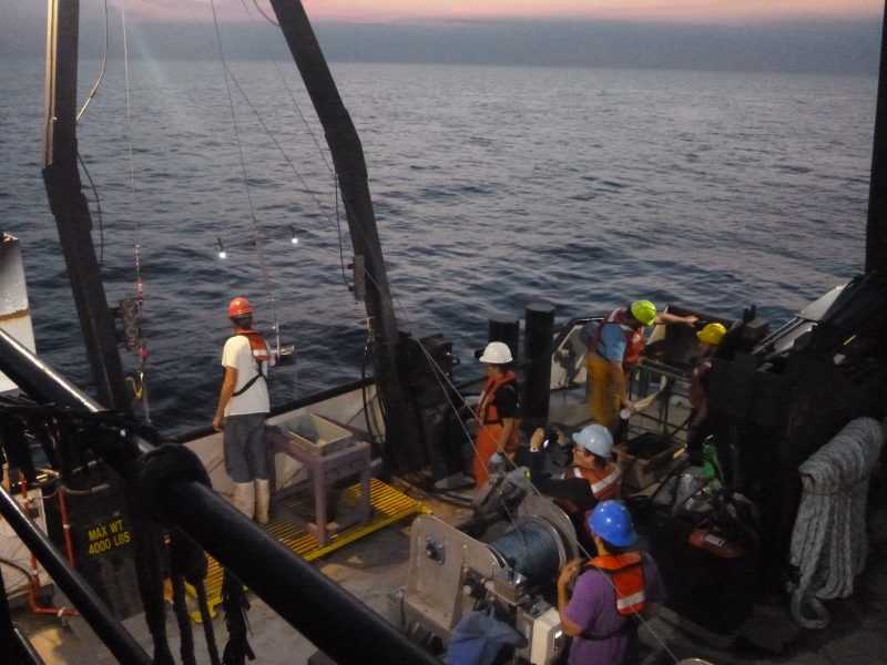 Several people work on the back deck of a large boat at twilight.