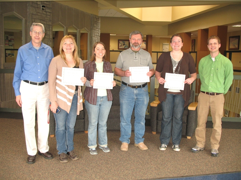 A group of six people posing for a picture. Four people hold up certificates