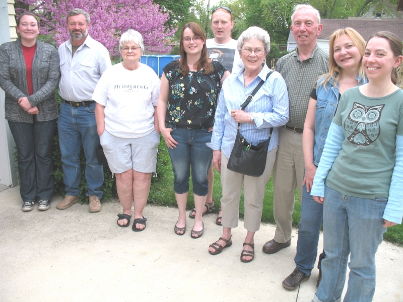 a group of eight people pose for a picture outside on a driveway