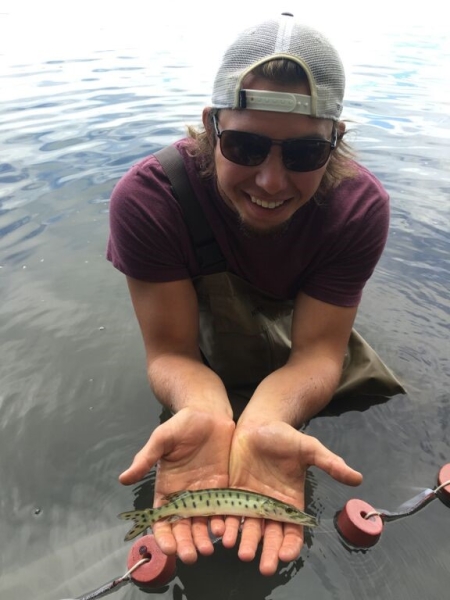 A person standing in water holds up a speckled fish on his outstretched palms