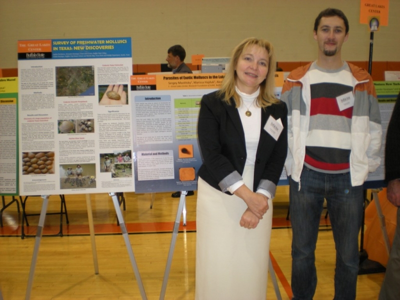 Two people pose for a picture in front of posters on easels