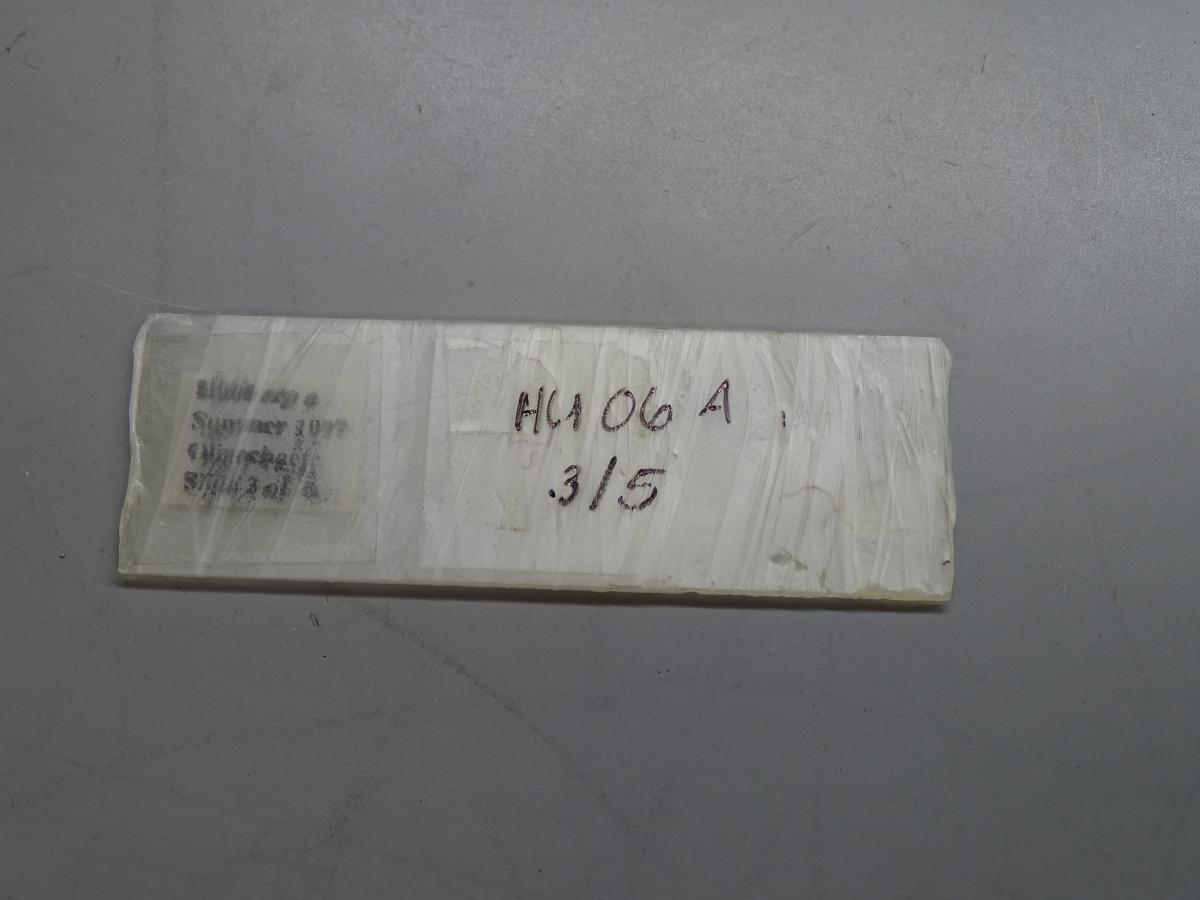 A microscope slide wrapped in film. The label is obscured, but there is writing on the film. 