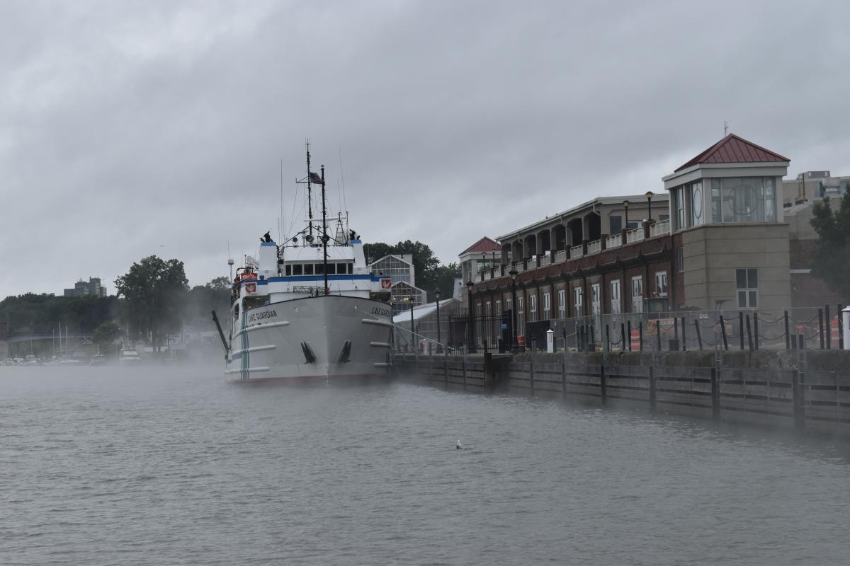 The front of a large white boat that is docked in a misty river.
