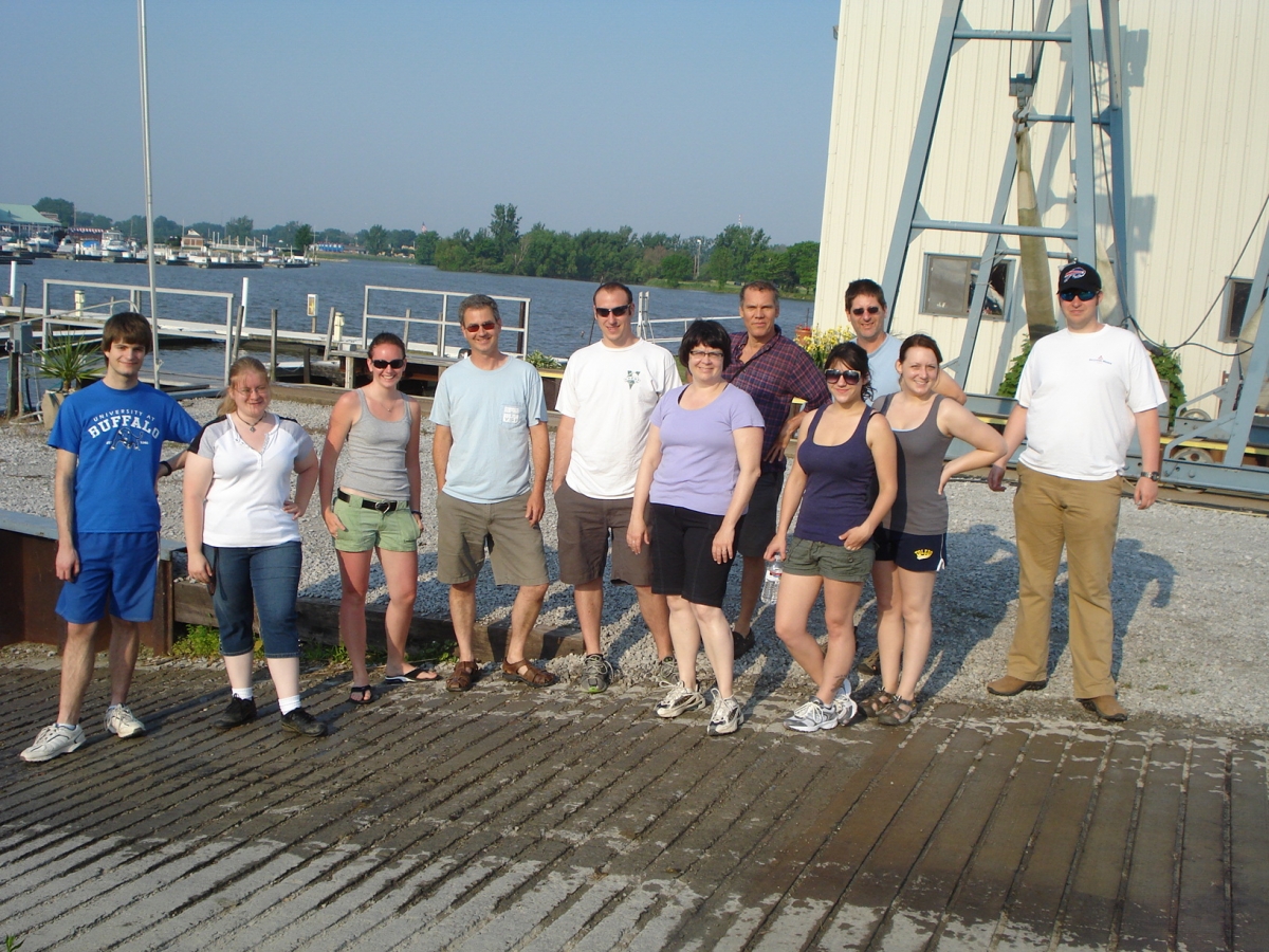 Eleven people stand for a picture near a boat launch.