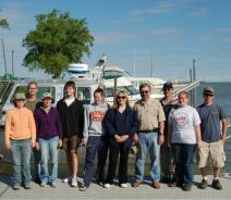 Ten people stand on a boat dock in front of a boat
