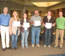 A group of six people posing for a picture. Four people hold up certificates