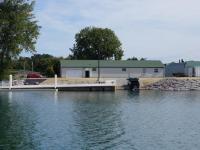 A white building with a green roof with a dock and boat launch, next to the water. A truck with a trailer is backed down the ramp toward the water.