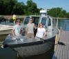 Three people stand for a picture at the front of a grey boat that's tied up to a dock.