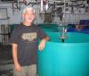 A person stands with their arm resting on a round green tank in a lab. Their shirt says "Arizona"