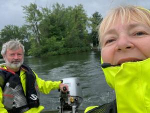 Two people in a selfie while one steers and outboard motor on a boat in the water.