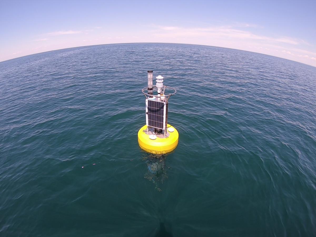 A buoy with meteorological equipment and solar panels on the open water. Picture taken with a fisheye lens since the horizon is warped into a convex curve.